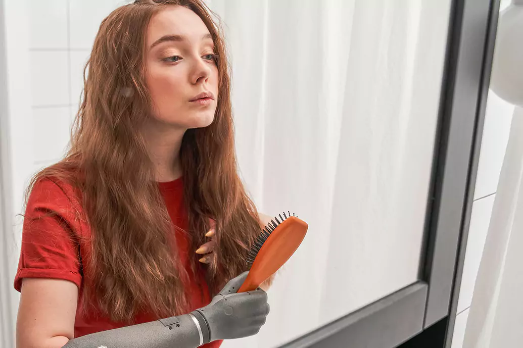 Disabled woman with amputated arm brushing hair in mirror