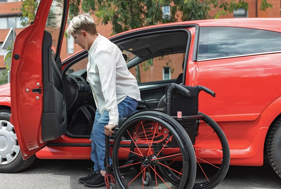 Disabled woman getting into wheelchair from car